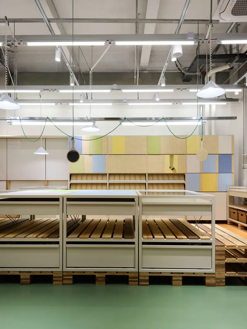 Low white metal display tables on wooden pallets under exposed ceiling ducts and fluorescent tube lighting