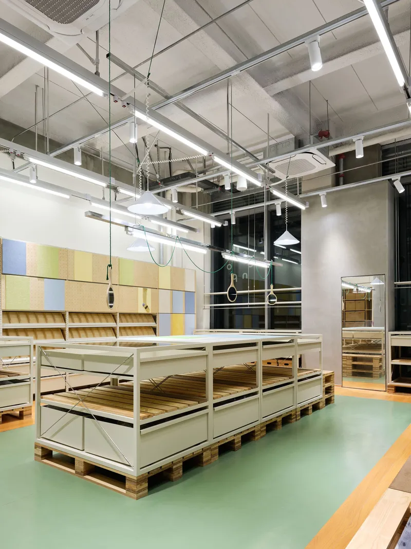Green rubber flooring meets pale wood zones around metal display tables beneath suspended linear lighting