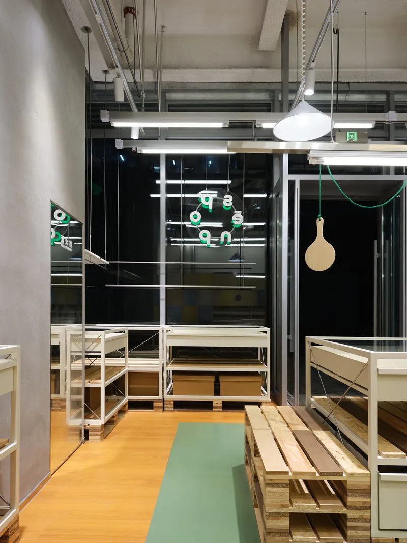 Night view through black glazed storefront showing illuminated interior with timber benches and pendant fixtures