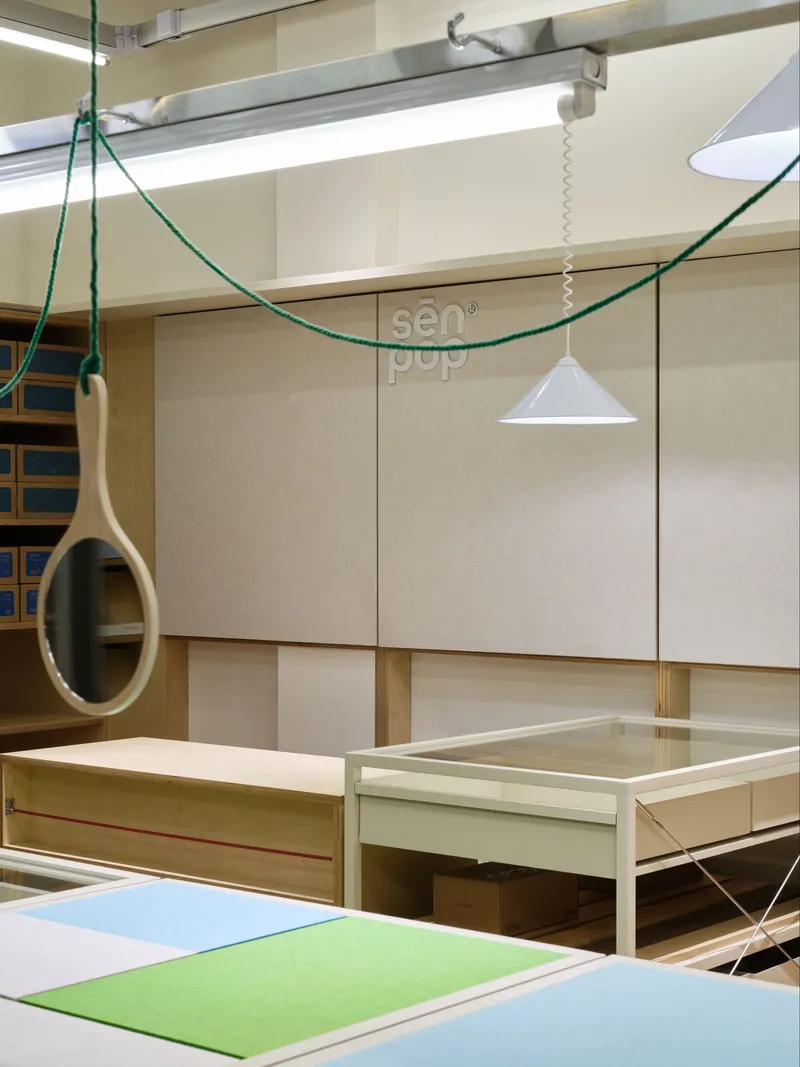 Interior view showing plywood shelving units and pendant lights suspended by green cables beneath fluorescent fixtures