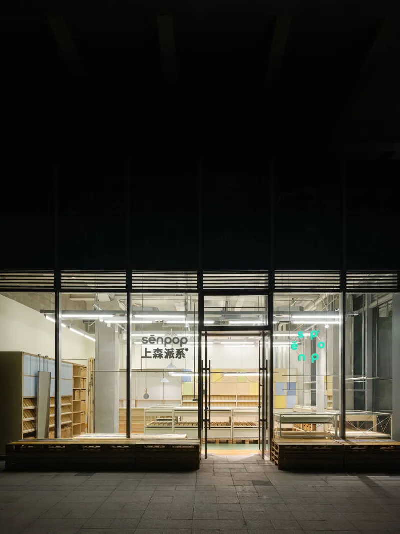 Street-facing storefront with floor-to-ceiling glass panels and black steel mullions illuminated at night