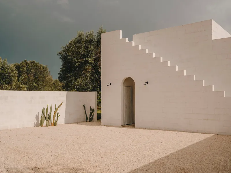 White rendered courtyard wall with stepped parapet and arched doorway flanked by cacti