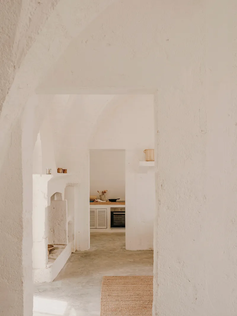 View through arched openings into kitchen with white plaster walls and concrete floor