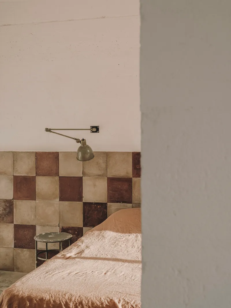 Partial view of chequered tile headboard with wall-mounted brass lamp beside plastered column