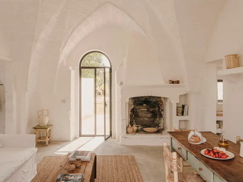 Vaulted living space with arched doorway, stone fireplace surround, and timber dining table under soft daylight