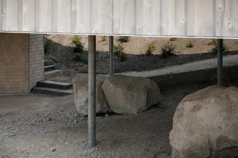 Exterior courtyard with steel columns, large boulders, gravel ground and planted slope