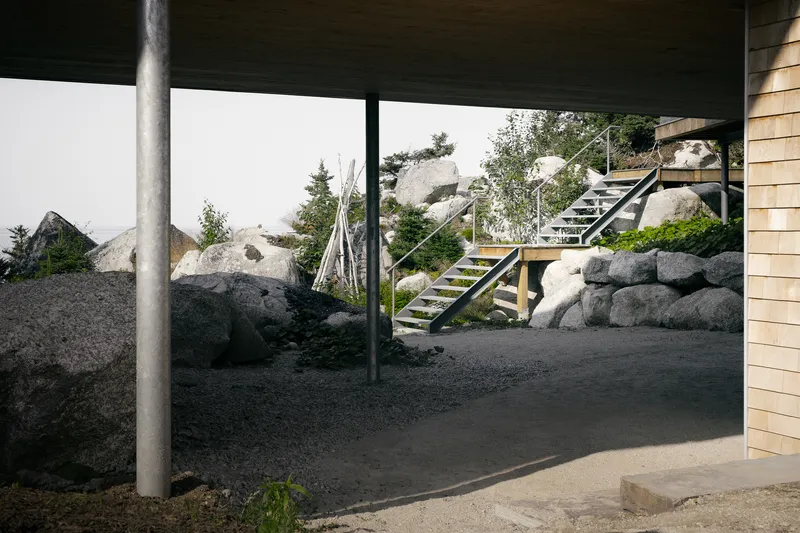 Covered outdoor space with steel column, exterior staircase and boulders under overcast sky