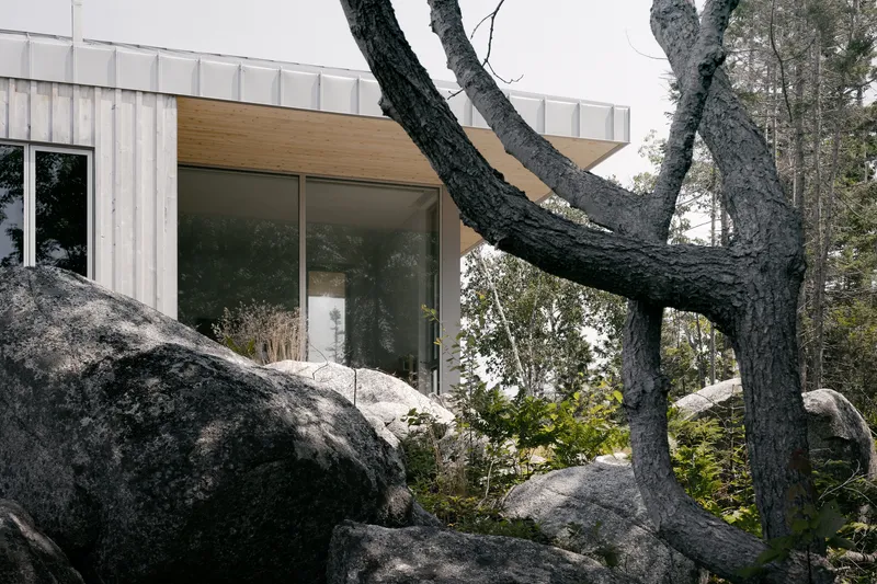 Glass facade opening framed by granite boulders and a charred tree trunk