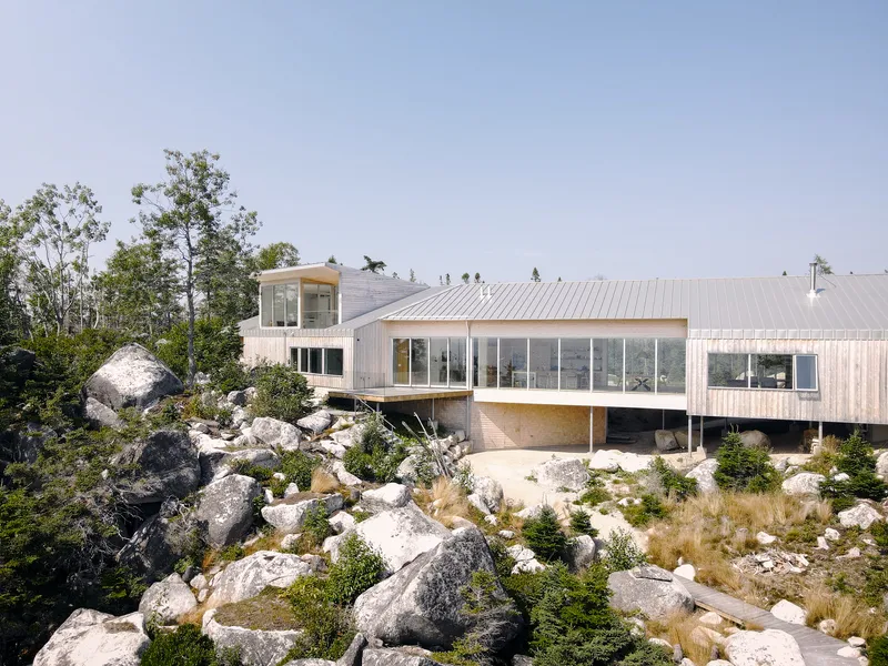 Metal-clad volume perched on a rocky outcrop surrounded by pine trees and native grasses