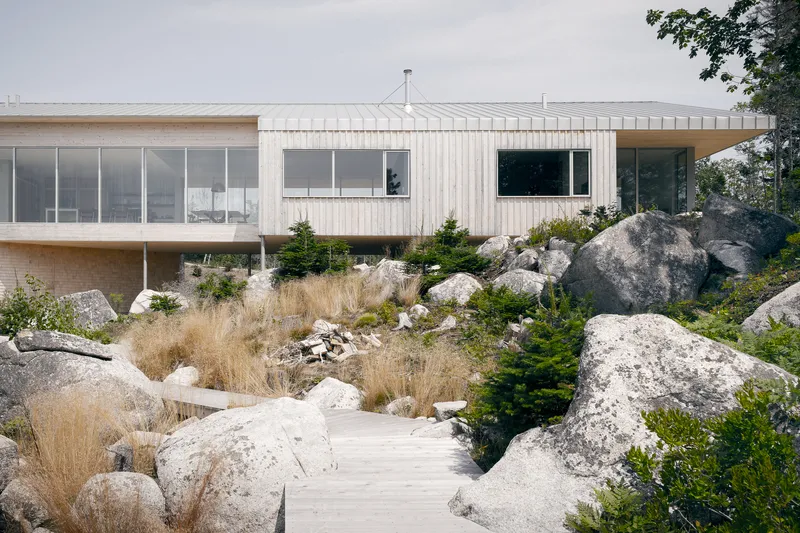 Timber deck threading through large granite boulders and native grasses below the glazed facade