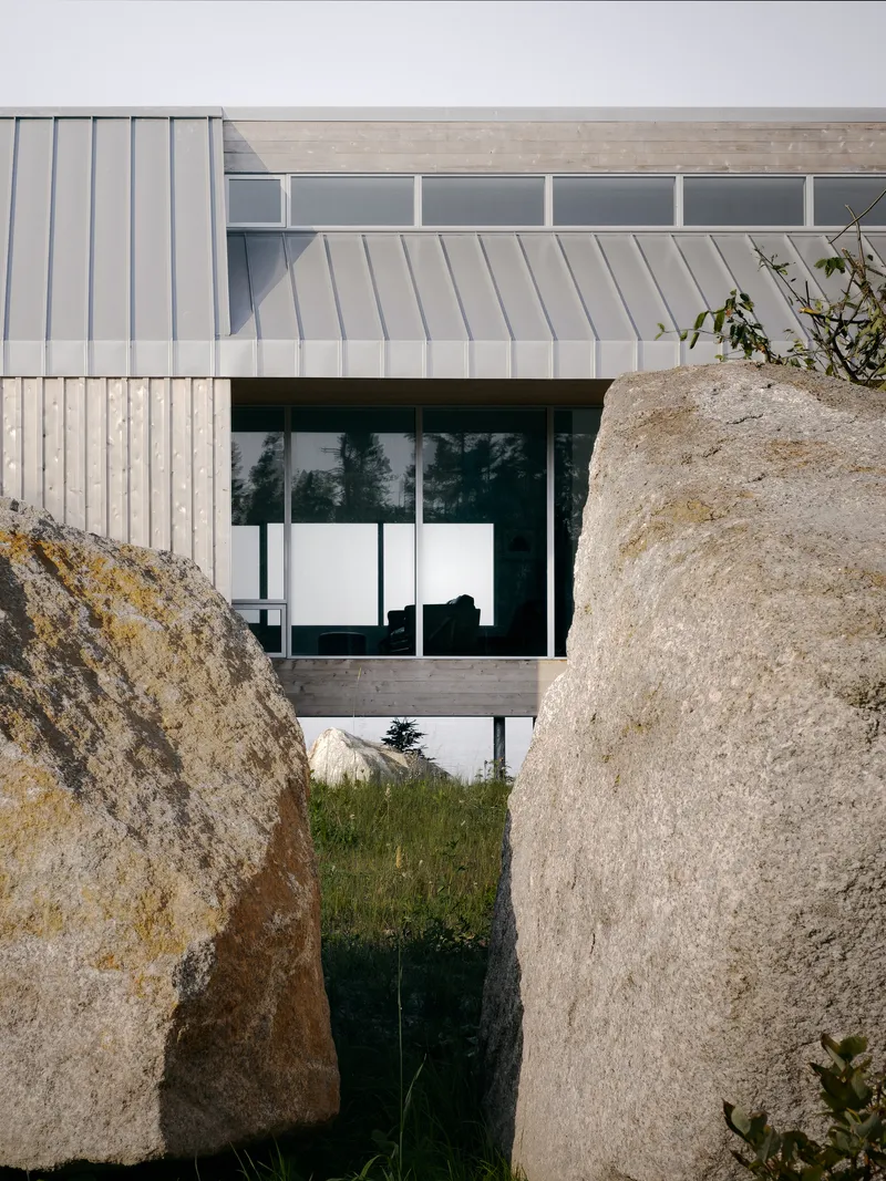 Vertical timber and metal panel facade framed between two weathered granite boulders