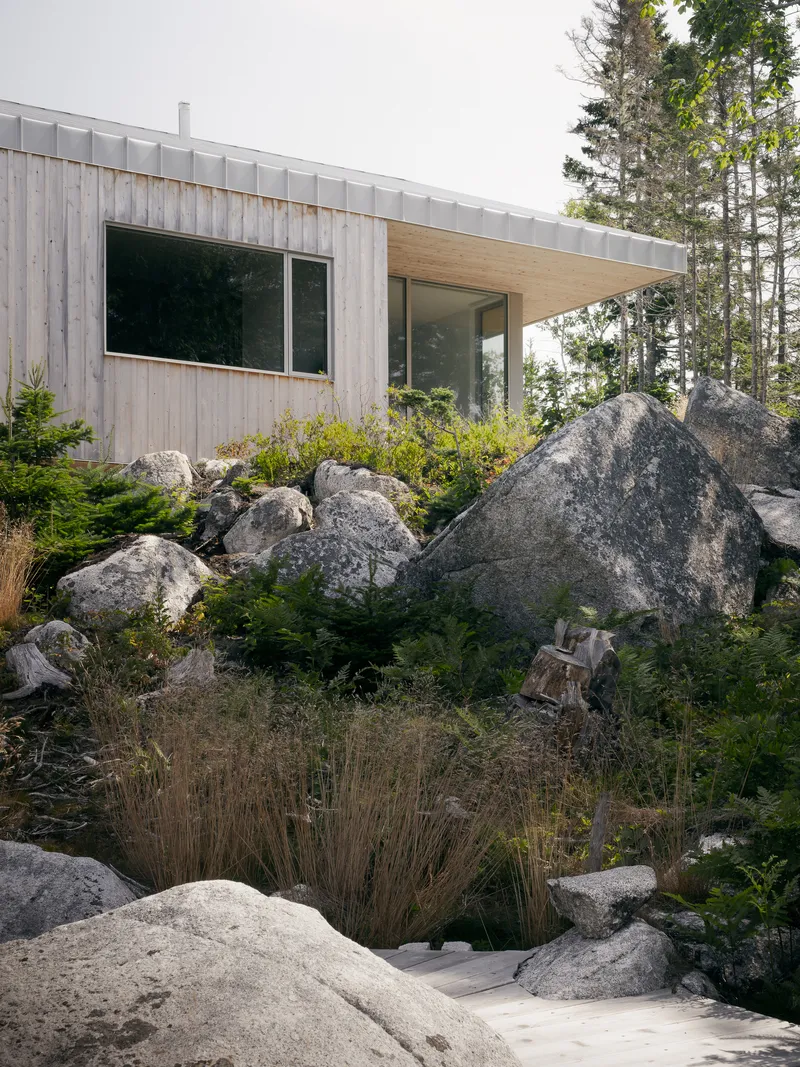 Timber-clad volume with metal seam roof nestled among granite outcrops and low plantings