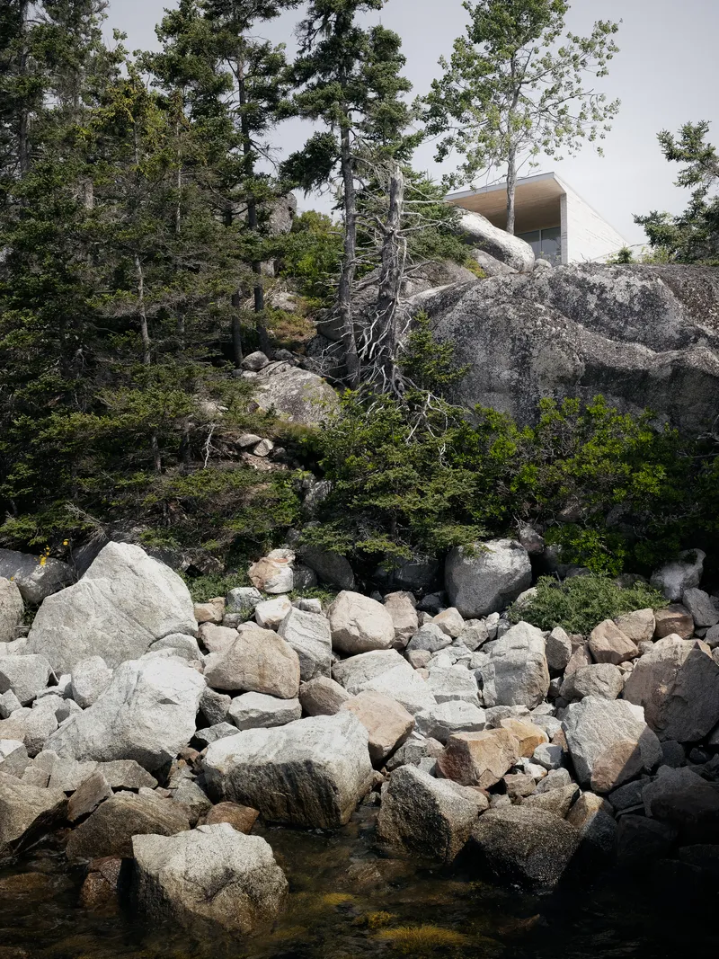 Distant view of cantilevered roof volume rising above a boulder-strewn water edge
