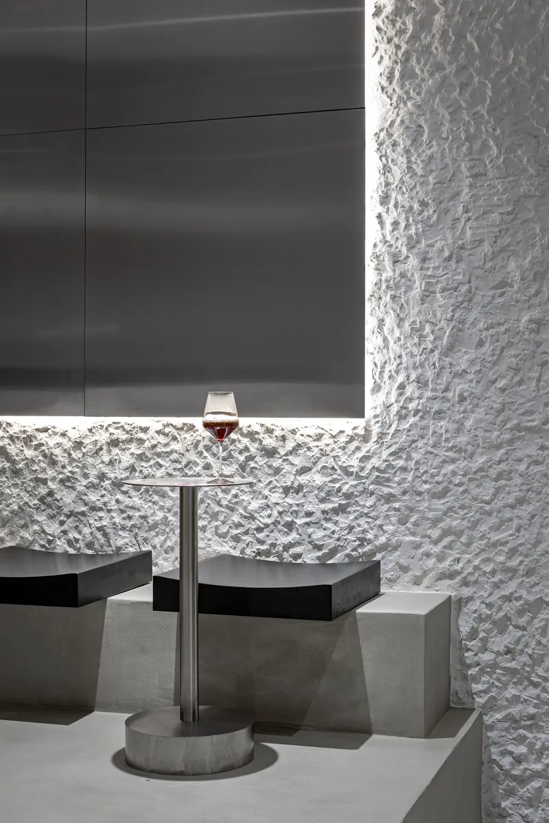 Concrete table with wine glass against textured white wall and backlit horizontal niche