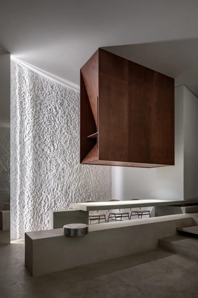 Cantilevered timber volume hovering above concrete counter with textured white wall beyond