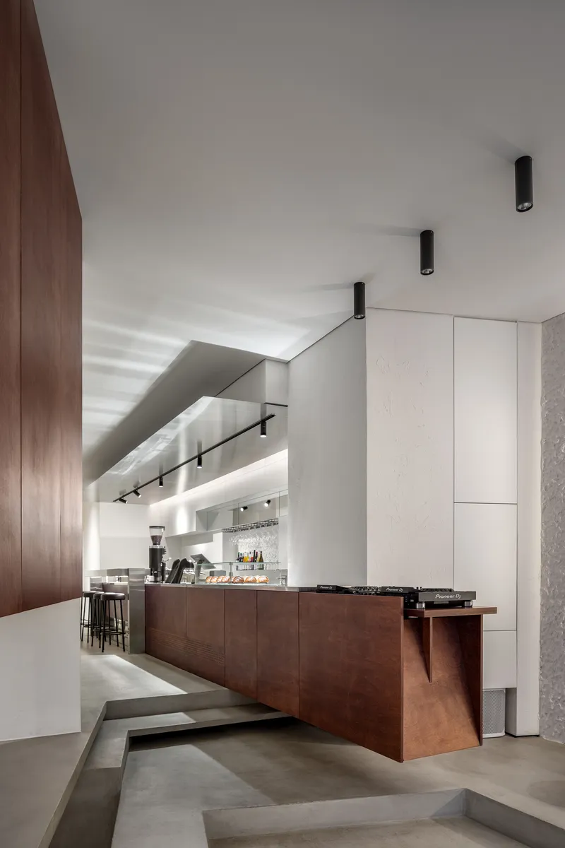 Cafe counter with dark timber cladding and cylindrical black ceiling fixtures under white soffit