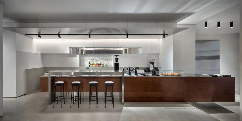Service counter with walnut base and four bar stools under linear ceiling lighting