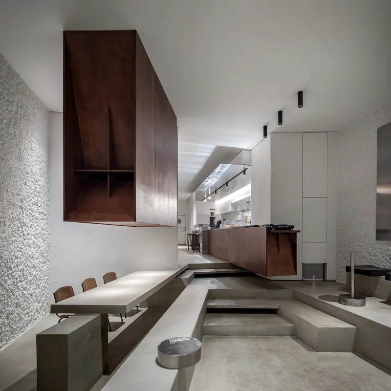 Split-level interior with stepped concrete seating and dark timber cabinetry suspended above the dining area