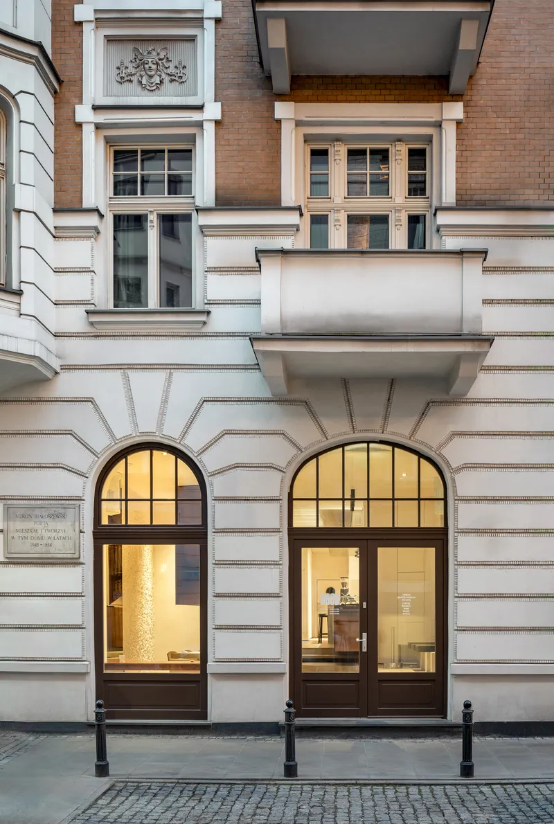 Street facade with arched entryways and rusticated stone base beneath dark-framed windows at dusk