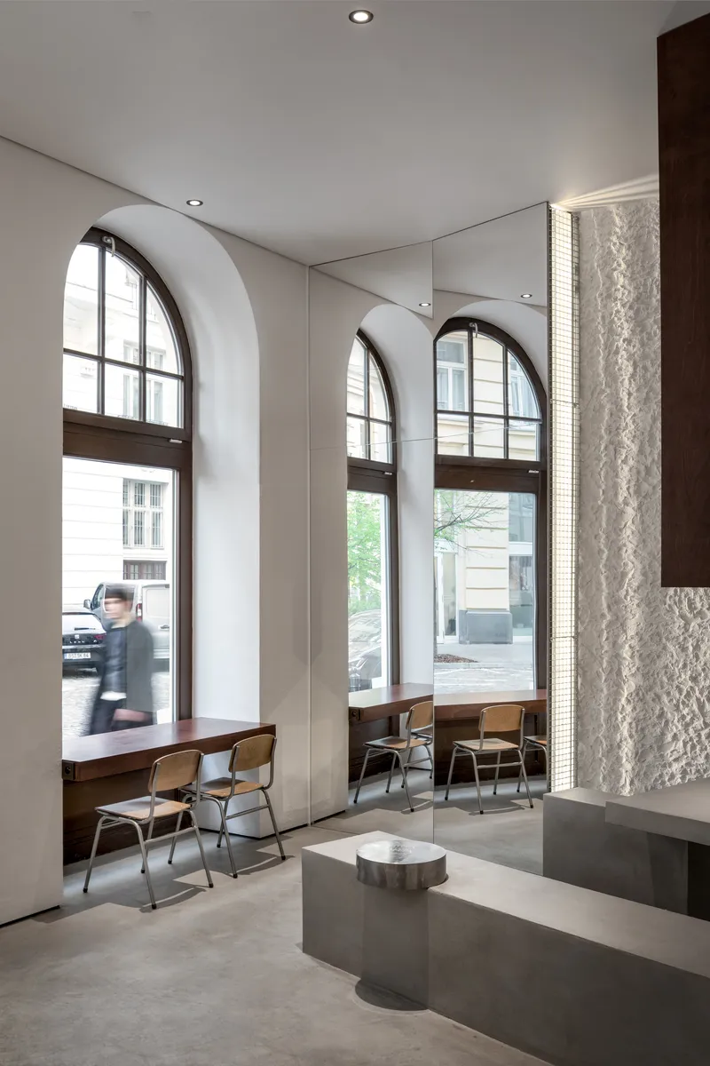 Tall arched windows with deep reveals overlooking the street, a figure passing by the seating below