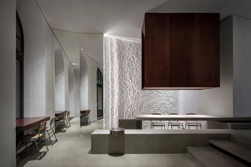 Backlit textured white panel beside a dark timber volume hovering over the concrete seating platforms