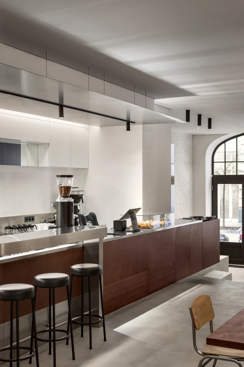 Coffee bar with dark timber base and white overhead cabinetry beneath linear suspended lighting