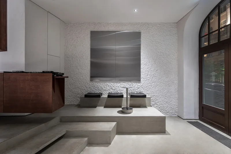 Concrete seating platform with three metal chairs facing a brushed steel wall panel