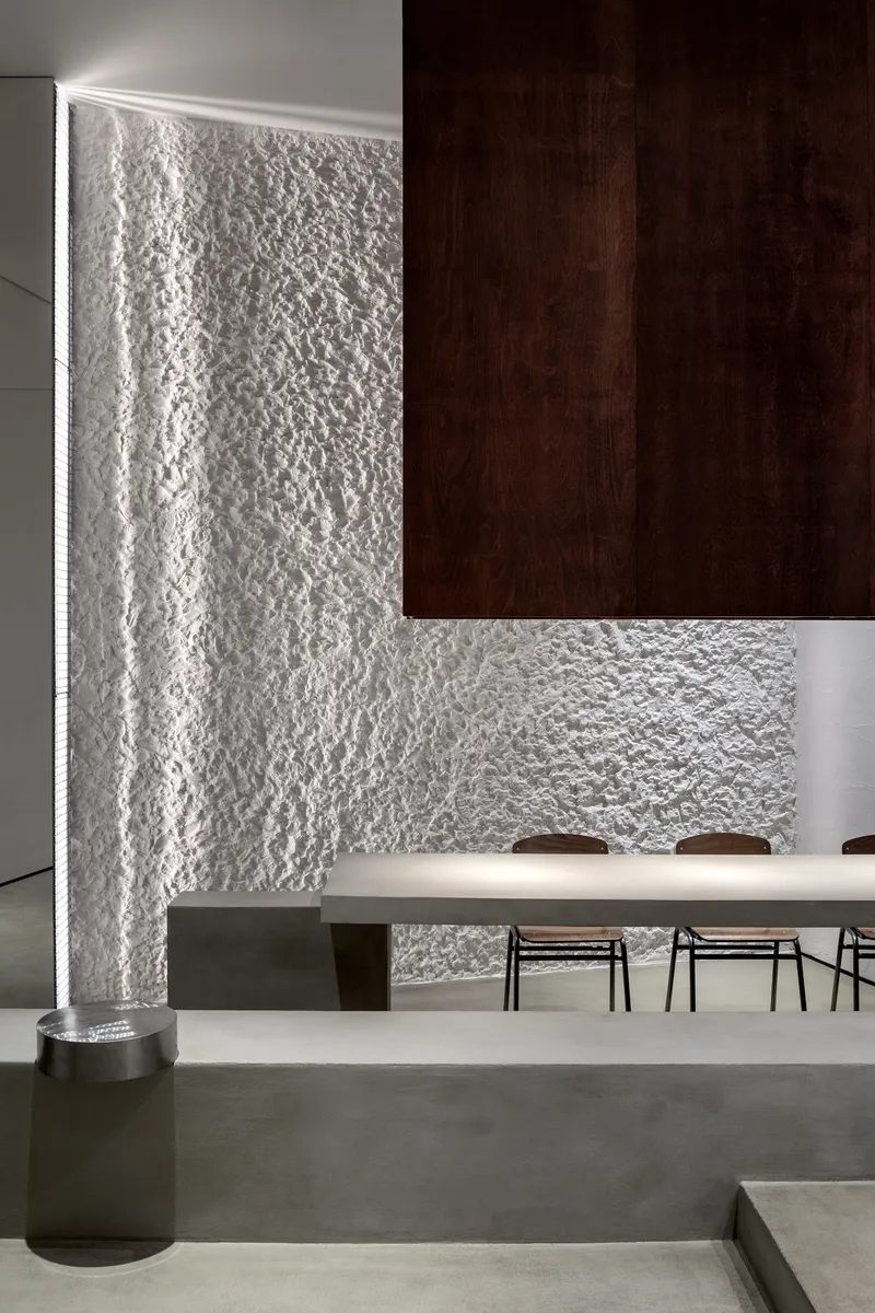 Backlit textured plaster wall meeting a cantilevered walnut cabinet above a dining table