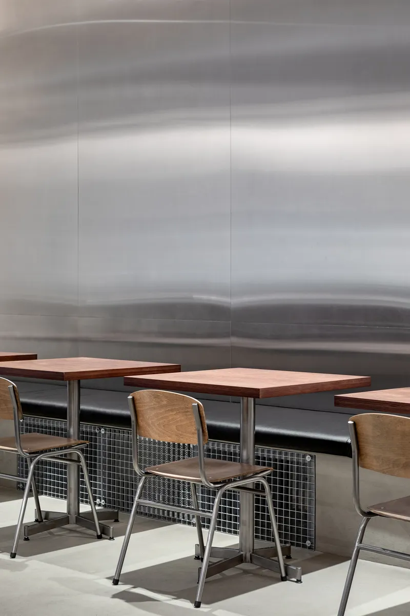 Cafe seating with wood tables and metal chairs against a brushed steel landscape mural
