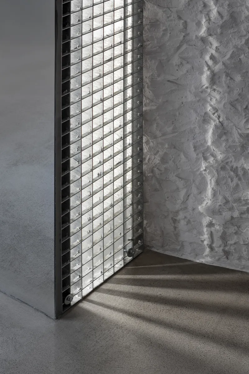 Glass block window casting diamond shadows on concrete floor beside a weathered plaster wall