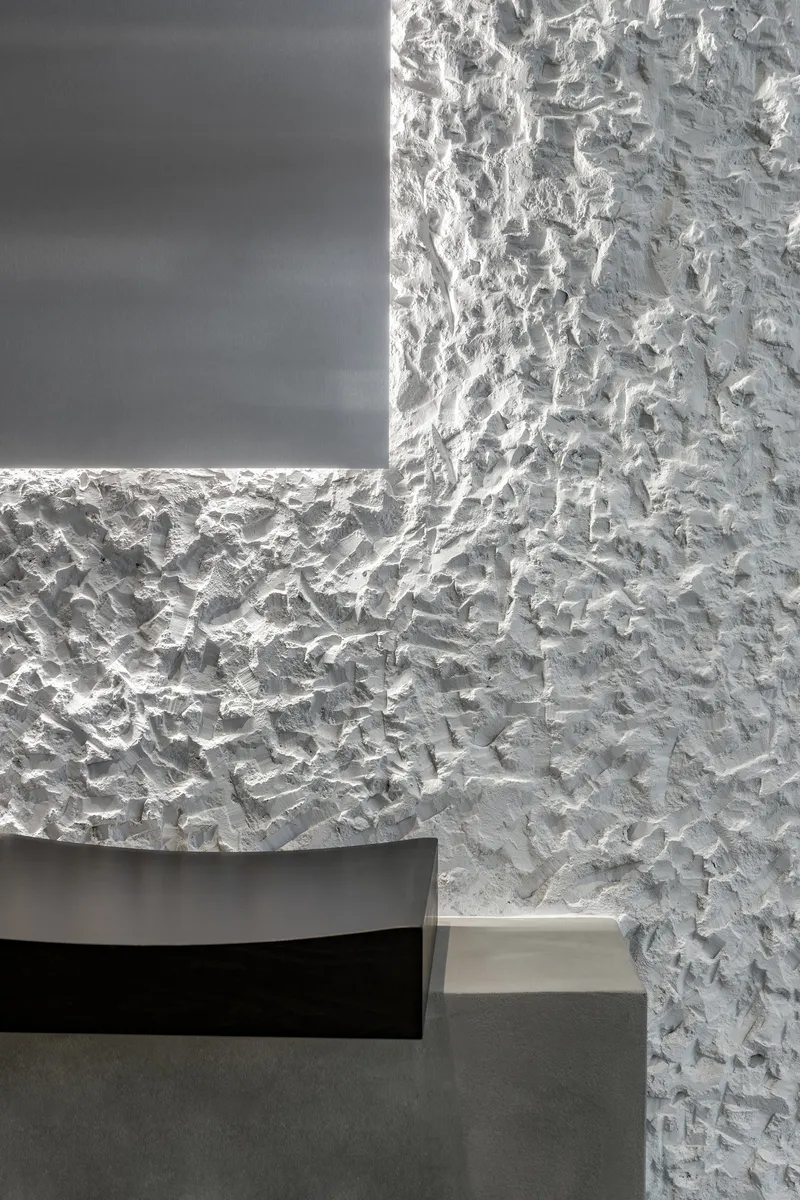Corner detail where rough white textured plaster meets a recessed dark panel with concealed lighting