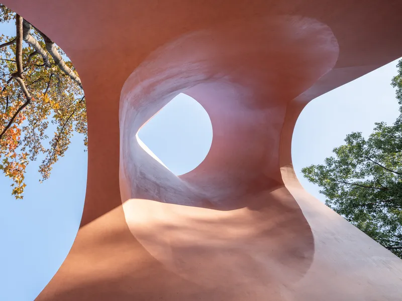 Looking up at twisted pink concrete columns forming organic openings framing sky and tree branches