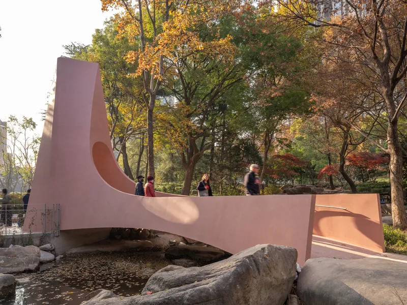 Side elevation of the pink bridge with pedestrians walking across during autumn foliage season