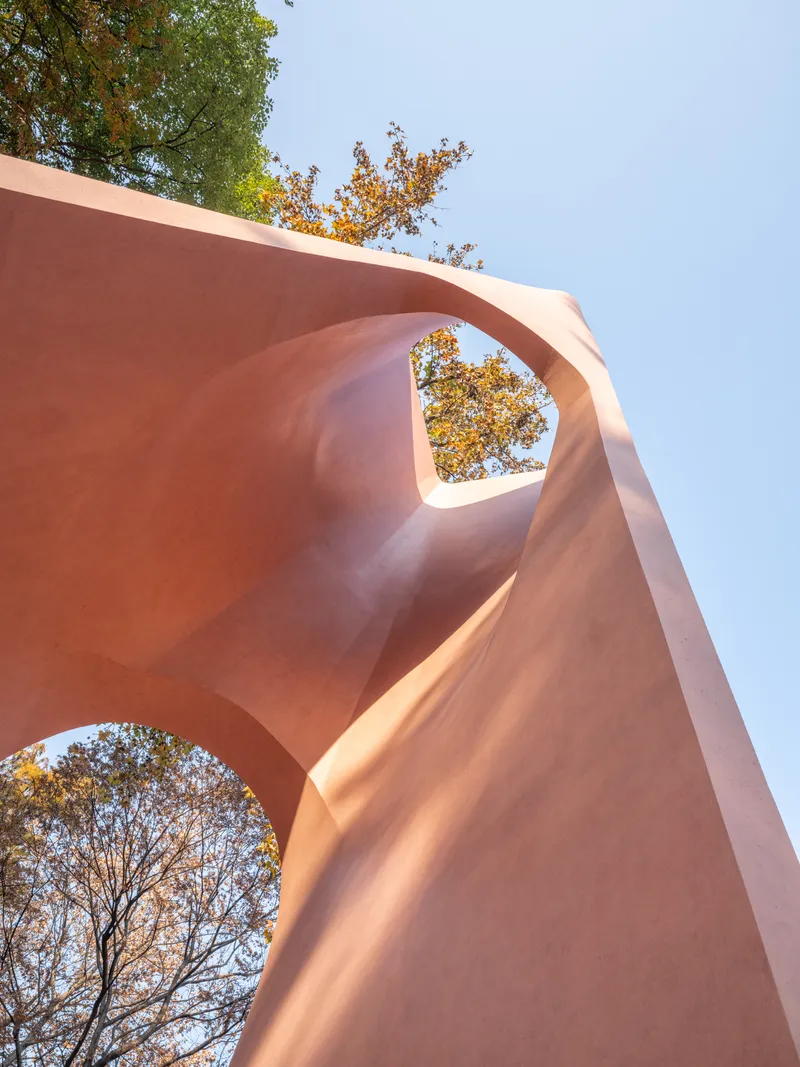 Looking up through two circular openings in a pink concrete sculptural structure with autumn foliage visible above