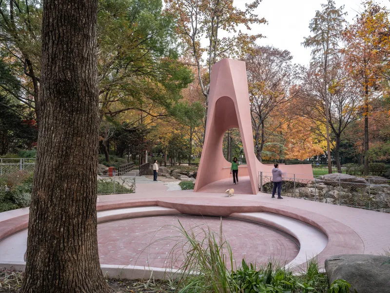 Curving pink concrete amphitheater steps descending to a circular platform beneath the arched gateway