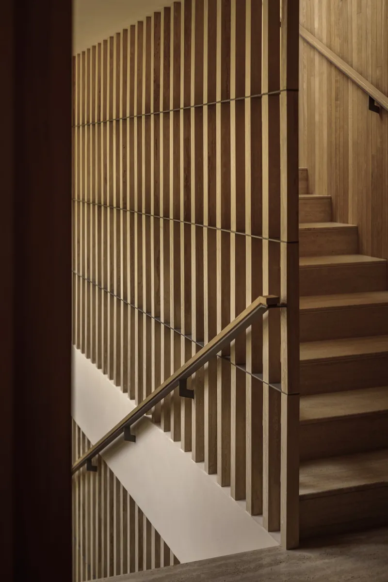 Timber staircase with vertical slat balustrade and bronze handrail alongside ascending steps
