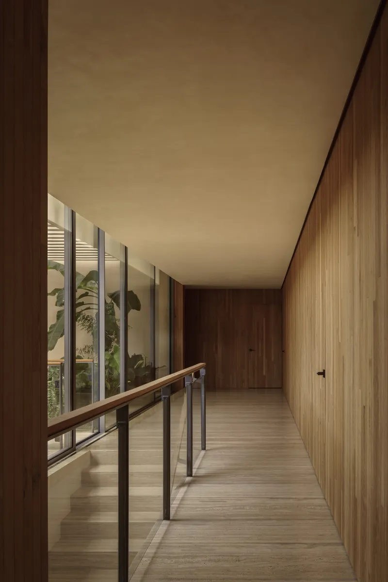 Upper-level hallway with timber walls and steel handrail overlooking courtyard with banana palms