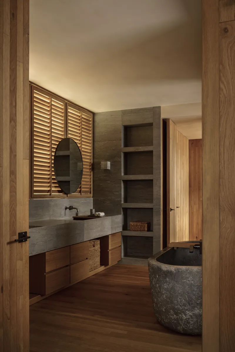Bathroom with concrete vanity, louvered timber screen, and stone soaking tub beneath wooden flooring