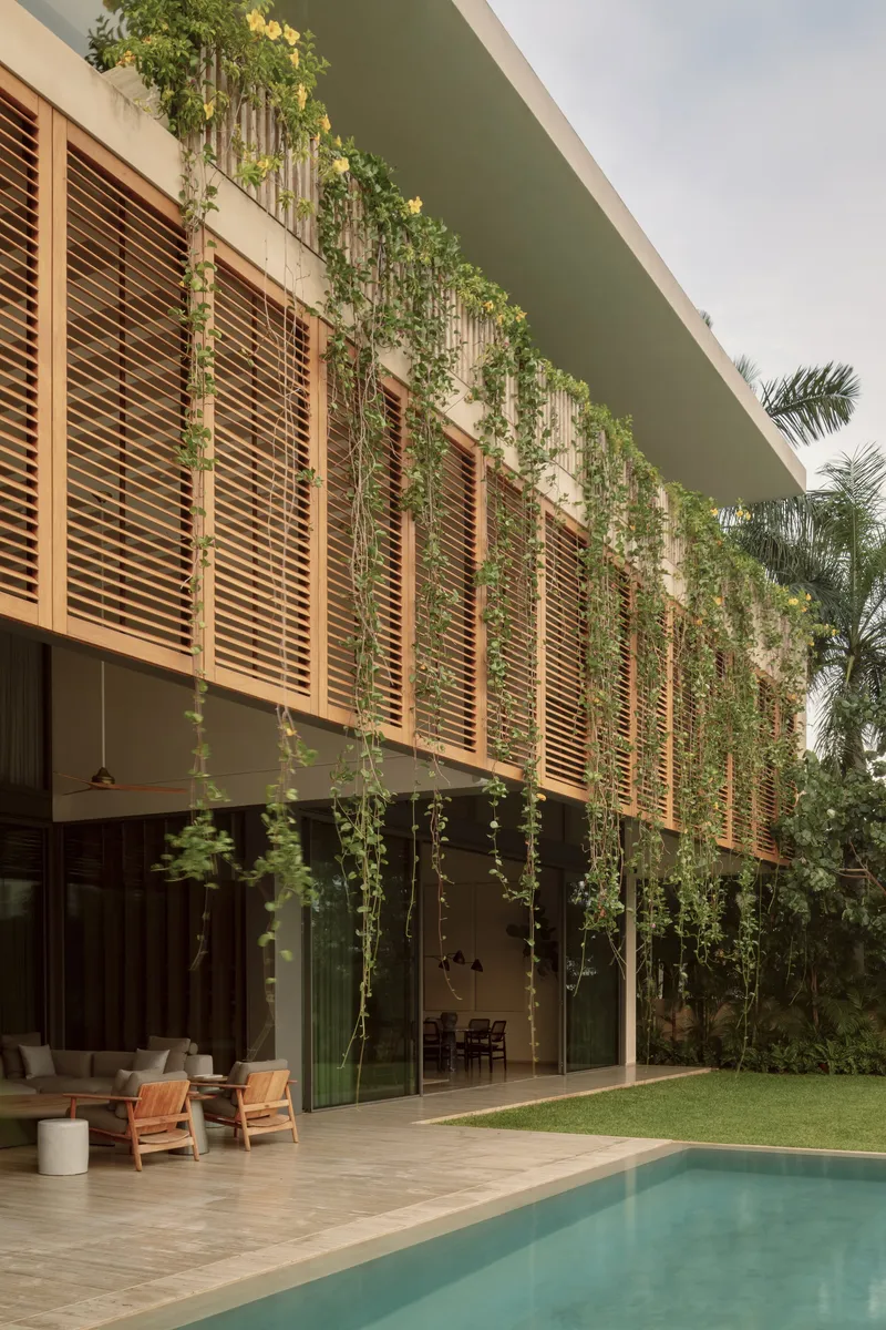 Garden facade with horizontal timber louvers and trailing vines above poolside terrace and lawn