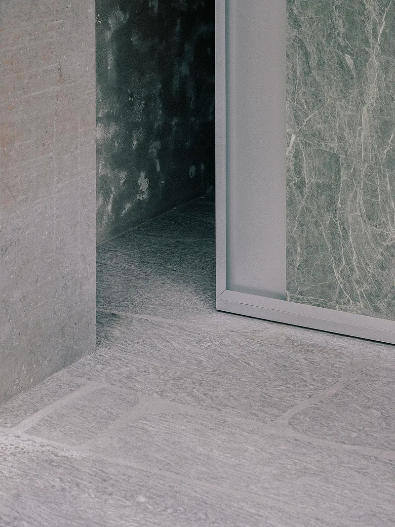 Corner threshold detail showing stone tile flooring meeting glass door and textured wall