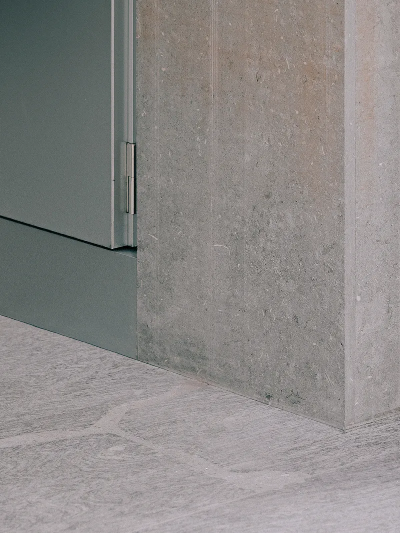 Corner detail where grey metal cabinet meets cast concrete wall and wood flooring