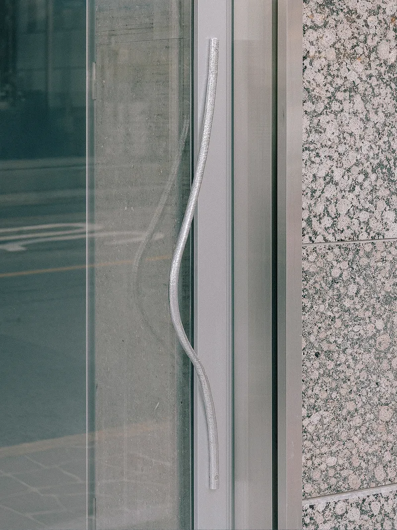 Glass door pull handle set against granite cladding and metal framing system