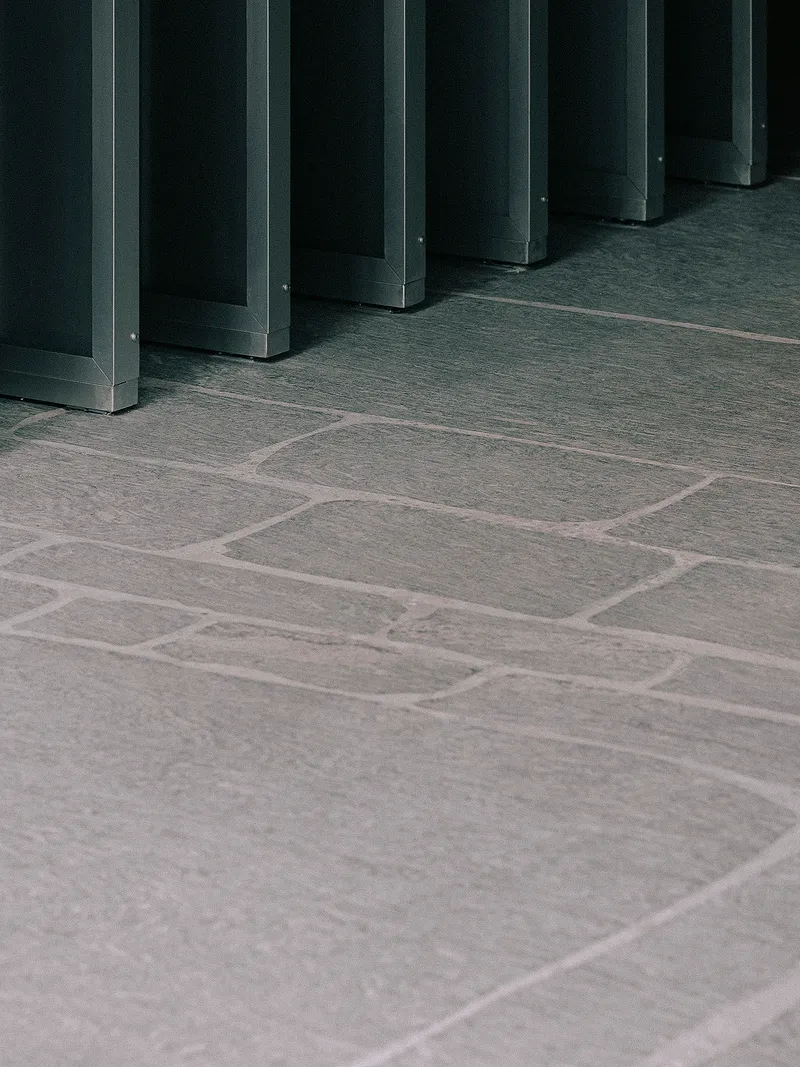 Stone tile floor meeting base of dark metal column framework in low light