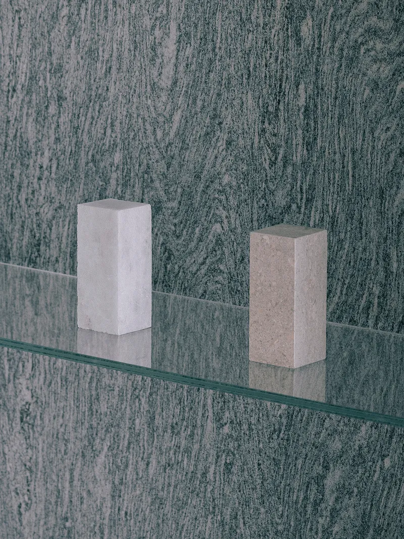 Glass shelf with two stone blocks mounted on textured dark wall panel