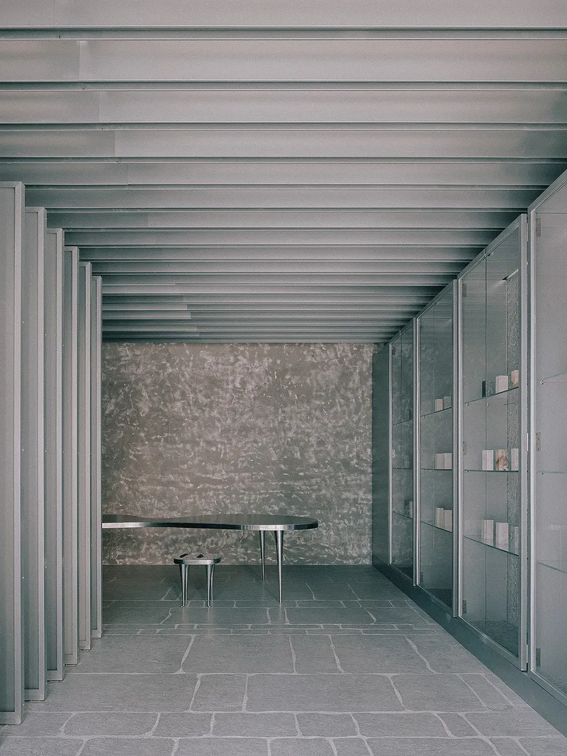 Interior colonnade with exposed metal beams, textured stone wall, dark table and floor-to-ceiling glazed partition