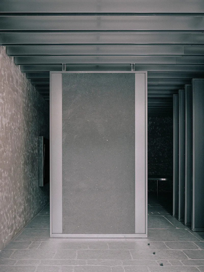 Pivoting metal-framed door panel set between textured concrete walls beneath a ribbed ceiling