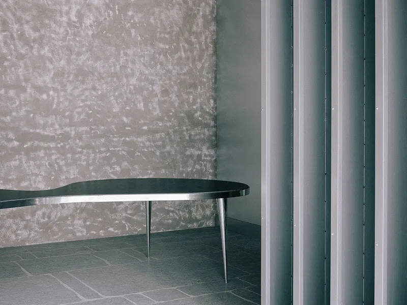 Detail of black curved tabletop with metal legs against textured wall and vertical metal columns