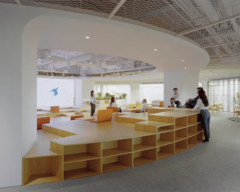 Curved ceiling soffit above modular plywood seating with integrated shelving and people gathered