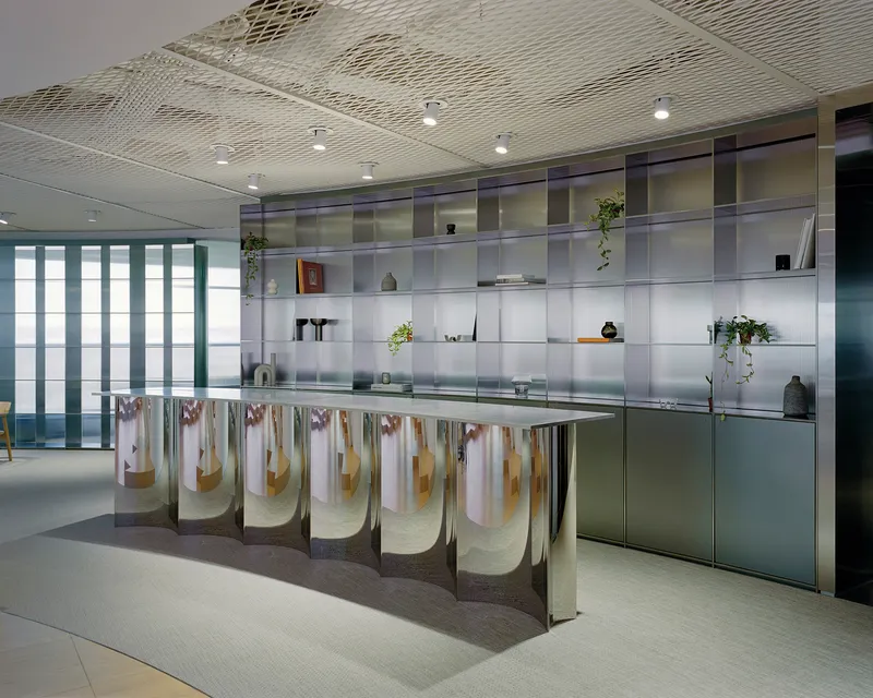 Kitchen island with pleated fabric skirt beneath translucent glass shelving wall displaying plants and objects