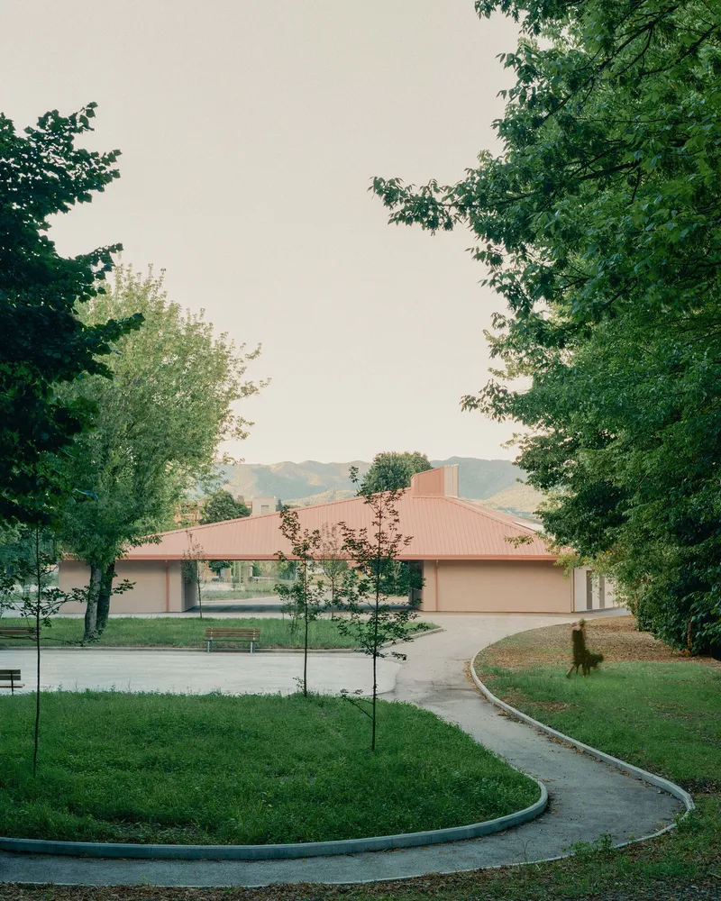 Entry approach with curved concrete pathway and planted beds leading to the hip-roofed pavilion